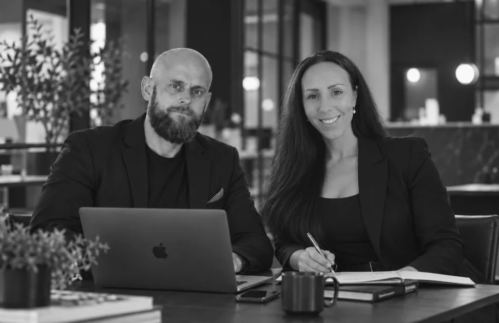 Timmi och Erika, grundarna av Quma webbyrå, vid ett skrivbord med laptop och anteckningsbok.